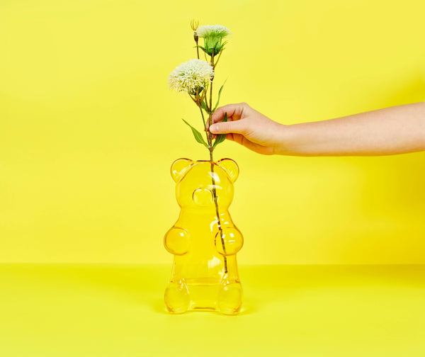 Yellow gummy bear-shaped vase with flowers against a yellow background