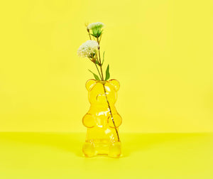 Yellow gummy bear-shaped vase with flowers on a yellow background