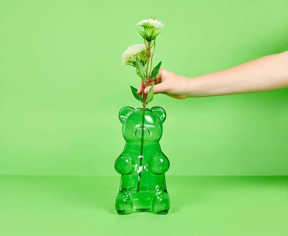 Green gummy bear-shaped vase with a hand holding flowers against a green background