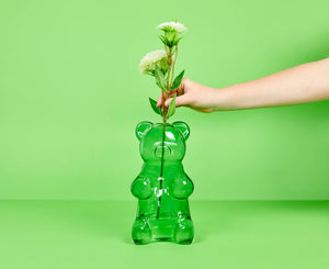 Green gummy bear-shaped vase with a hand holding flowers against a green background