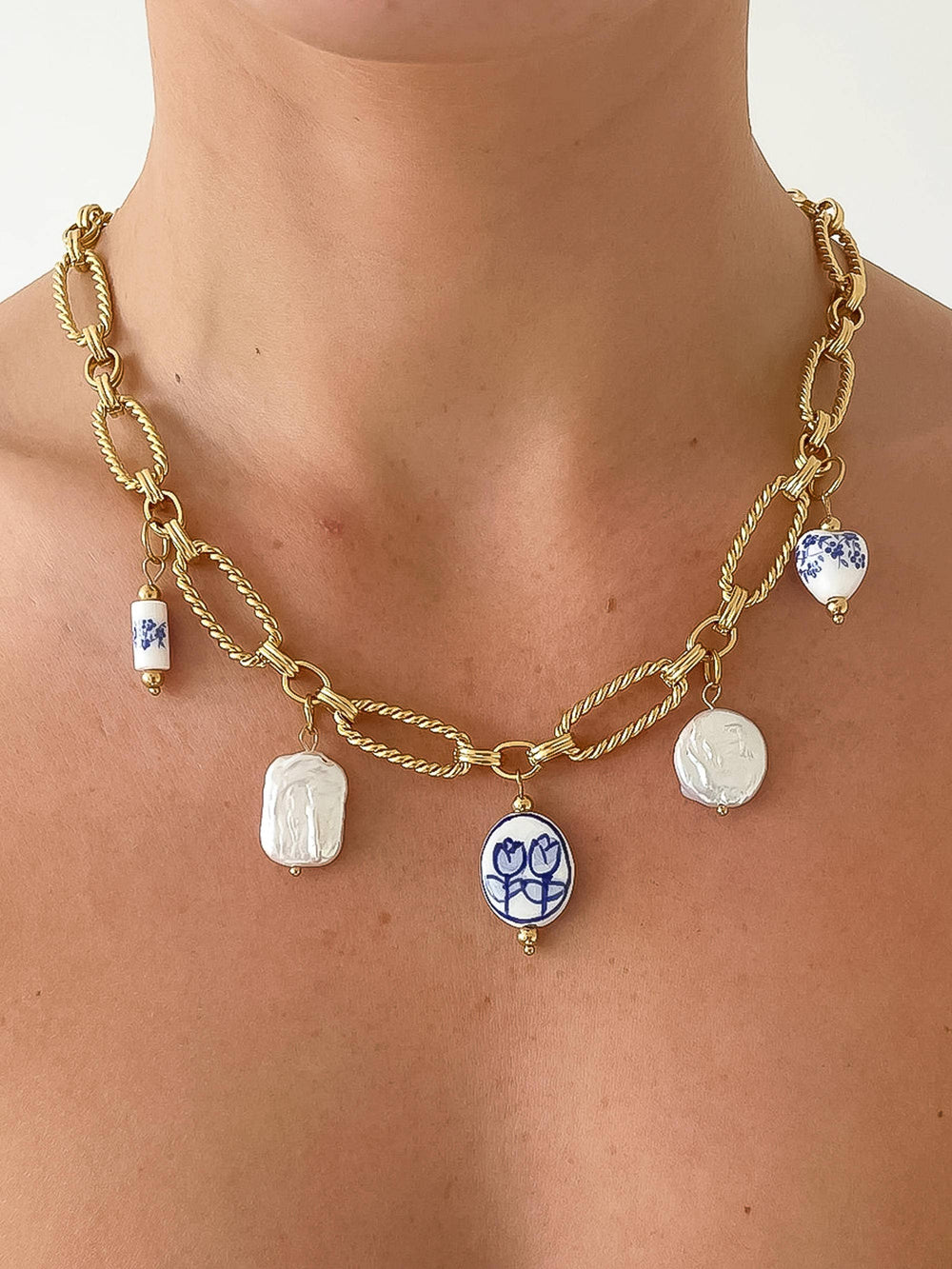 Gold chain necklace with ceramic charm pendants on a person wearing a white top.