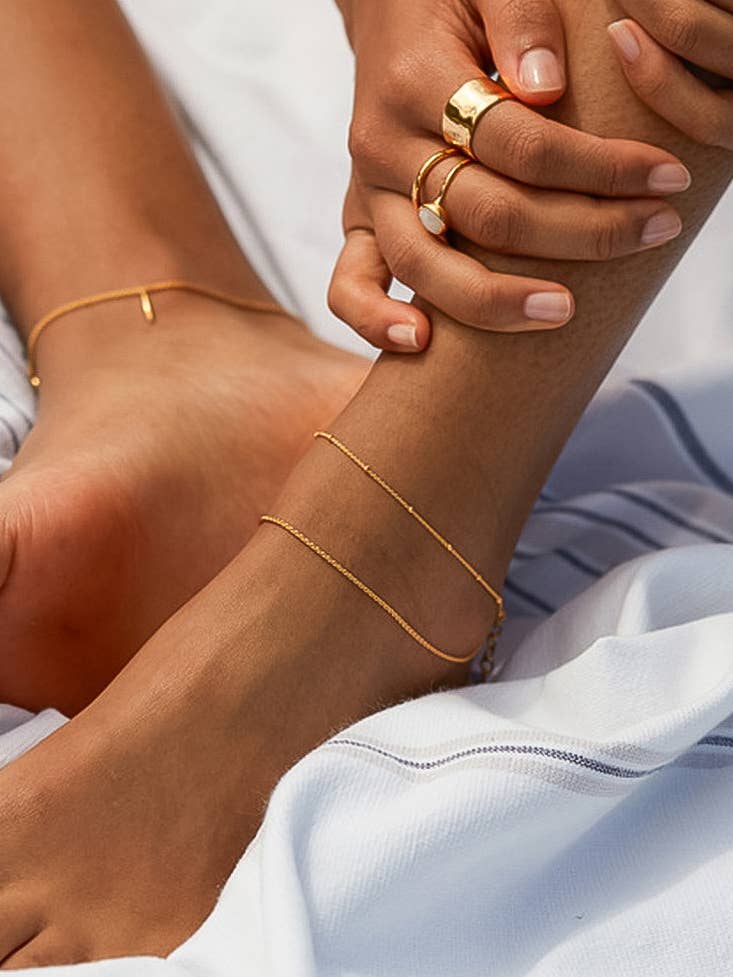 Close-up of a person's feet with gold anklets and rings on a white background
