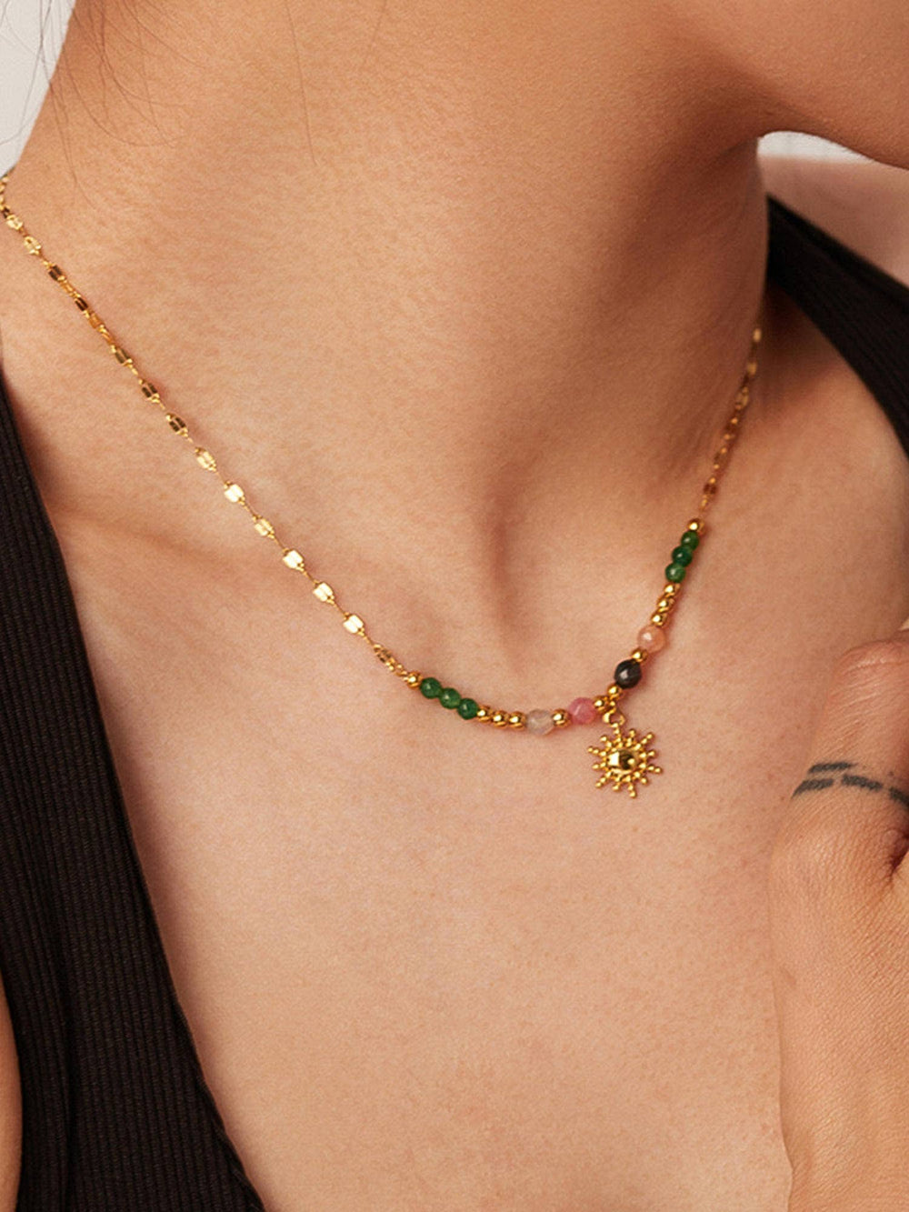 Gold necklace with green and red beads and a sun pendant on a person's neck.