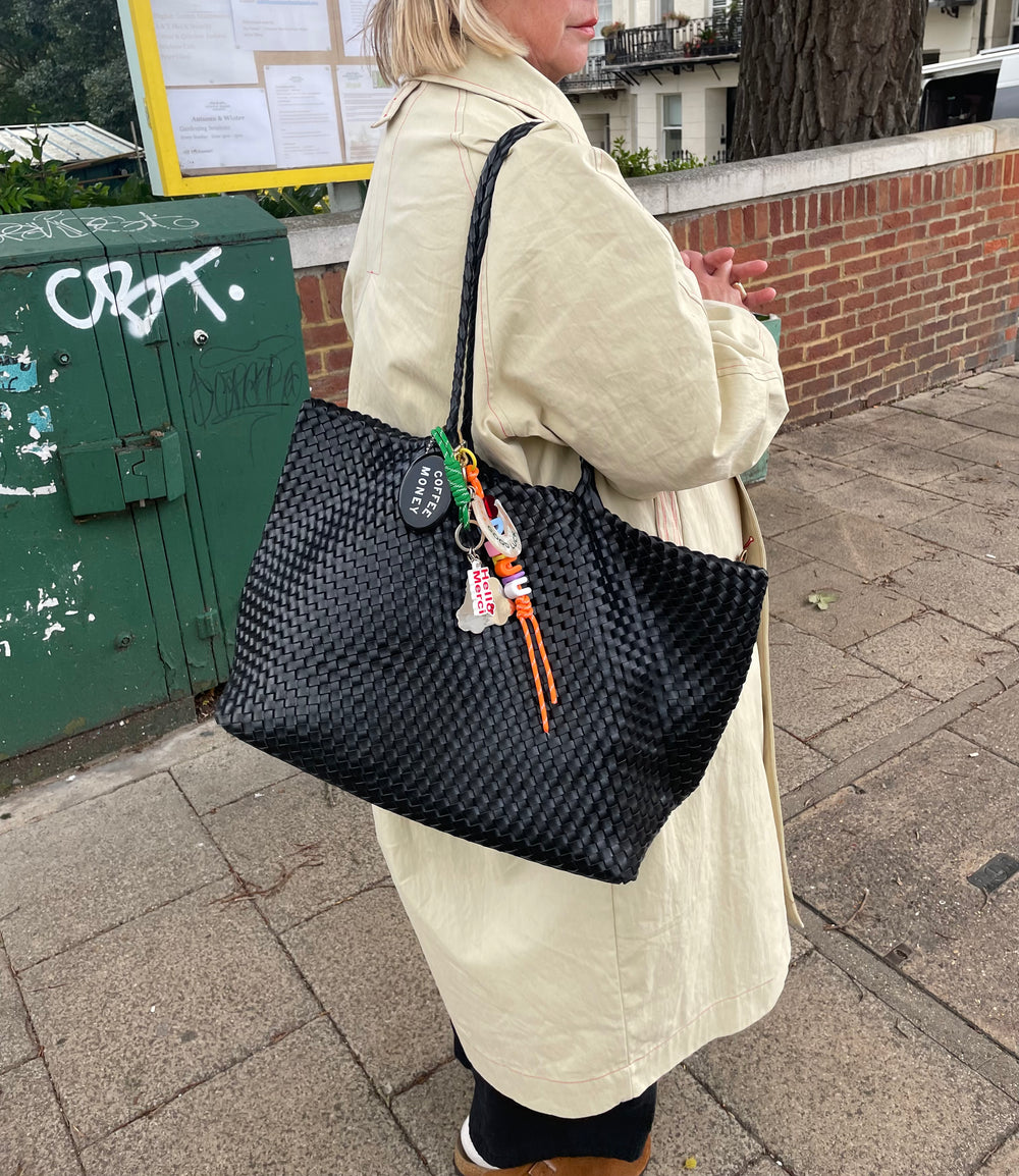 Person holding a black woven handbag on a pavement