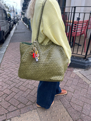 Person holding a textured green tote bag with a keychain on a sidewalk.