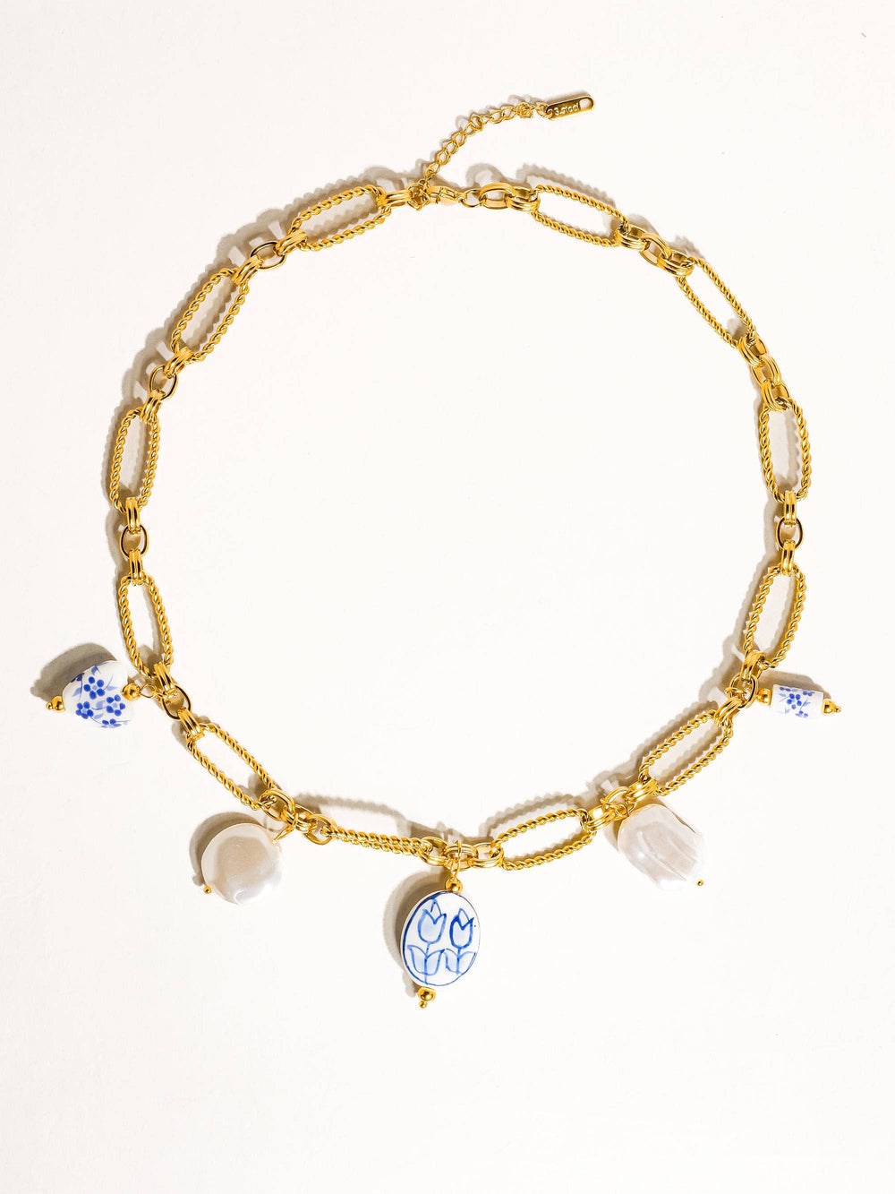 Gold chain necklace with ceramic charm pendants on a person wearing a white top.