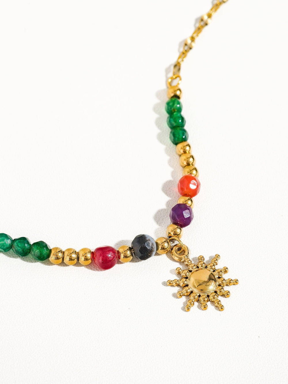 Gold necklace with green and red beads and a sun pendant on a person's neck.