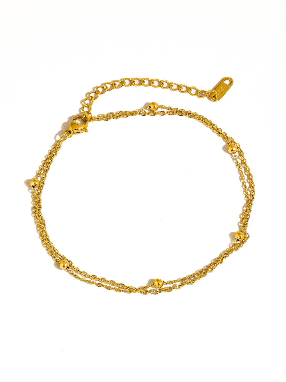 Close-up of a person's feet with gold anklets and rings on a white background
